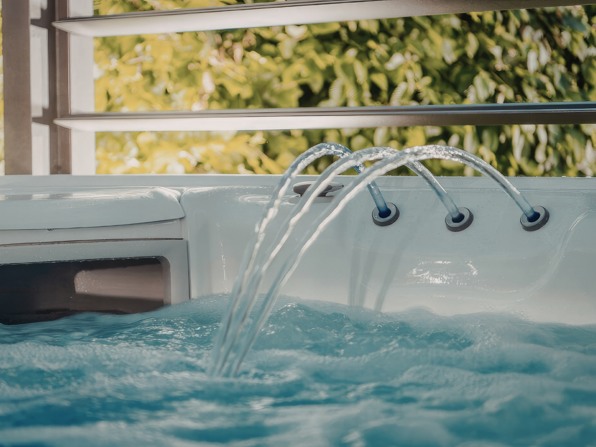 Close-up of hot tub water jets flowing into a bubbling spa with sunlight and greenery in the background